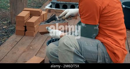 Ein Mann baut eine Mauer. Brick hat die Lösung aufgetragen. Bau eines Ziegelhauses. Stockfoto