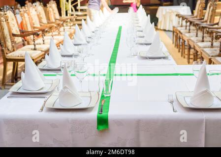 Langer Tisch mit Teller, Brille, Servietten und Stühlen Stockfoto