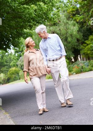 Sie laufen immer noch und halten Händchen. Ein liebevolles Seniorenpaar, das spaziert. Stockfoto