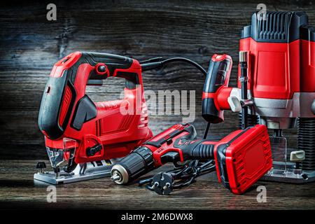 Elektrische Handwerkzeuge rote kabelgebundene Stichsäge Akku-Bohrmaschine und kleine Tauchfräsmaschine tragbarer Mini-Holzfräser auf altem Holzhintergrund Stockfoto