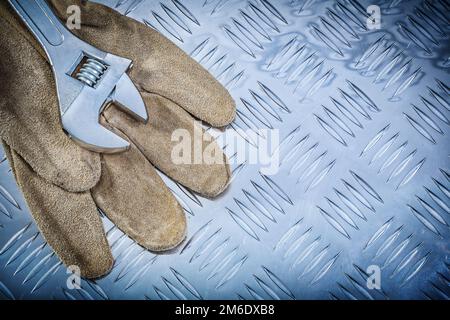 Sicherheitshandschuhe aus Leder verstellbarer Schraubenschlüssel auf kanalgeführtem Metallblech Baukonzept. Stockfoto