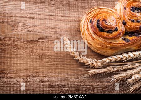 Rosinenbrötchen, Weizenohren auf Eichenholzbrettern, Speisen- und Getränkekonzept Stockfoto