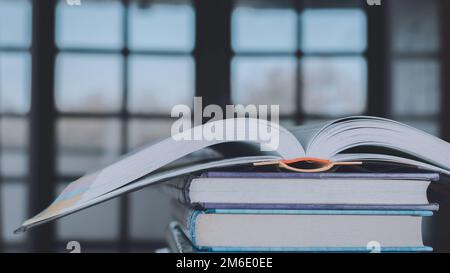 Stapel oder Stapel alter Bücher auf einem Holztisch. Lern-, Ausbildungs- und Studienkonzept. Einer von ihnen öffnet sich mit Kopierraum. Stockfoto