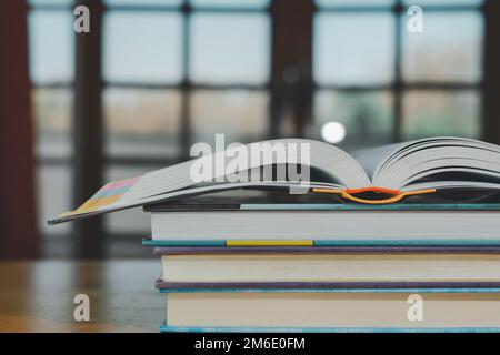 Stapel oder Stapel alter Bücher auf einem Holztisch. Lern-, Ausbildungs- und Studienkonzept. Einer von ihnen öffnet sich mit Kopierraum. Stockfoto