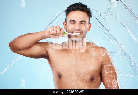 Gesicht, Wasserspritzer und Mann mit Zahnbürste zur Reinigung im Studio auf blauem Hintergrund. Zahnverblendungen, Hygiene und Porträt des glücklichen männlichen Modells Stockfoto