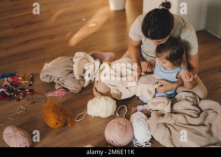 Draufsicht einer Frau mit ihrer kleinen Tochter, die mit einer Lochnadel mit schwarzem Faden an einer abstrakten Stickerei aus Gelb, Grün und arbeitet Stockfoto