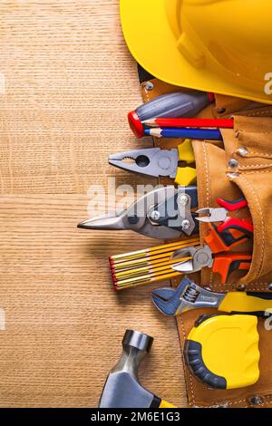 Bauwerkzeuge im Werkzeuggürtel Hammer Bandschlüssel Zange Cutter Bleistiftschraubendreher Helm auf Holzbrett Stockfoto