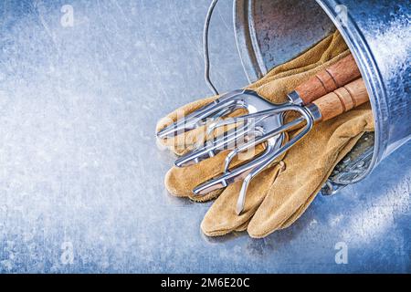 Verzinkter Eimer Metallrechen Gabel Lederhandschuhe auf metallischem Hintergrund. Stockfoto