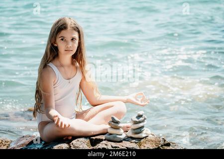 Eine Frau mit Tochter hat eine Biltsteinpyramide am Meer an einem sonnigen Tag auf blauem Meereshintergrund. Frohe Familienferien. Kieselstrand, ruhiges Meer. Konzept Stockfoto