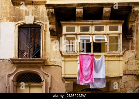 Bunte Kleidung oder Wäsche, die auf einer in Malta fotografierten Schnur getrocknet wird, einer Fassade eines historischen Gebäudes im Hintergrund Stockfoto