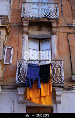 Bunte Kleidung oder Wäsche, die auf einer in Malta fotografierten Schnur getrocknet wird, einer Fassade eines historischen Gebäudes im Hintergrund Stockfoto