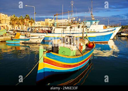 Traditionelle Fischerboote luzzu im Dorf Marsaxlokk in Malta, in leuchtenden Farben - blau, rot und gelb. Warmes Sonnenlicht am Nachmittag Stockfoto