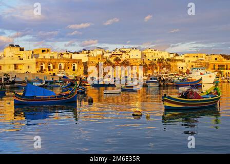 Traditionelle Fischerboote luzzu im Dorf Marsaxlokk in Malta, in leuchtenden Farben - blau, rot und gelb. Warmes Sonnenlicht am Nachmittag Stockfoto
