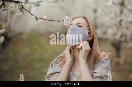 Frau zwischen blühenden Bäumen. Mädchen in einer medizinischen Maske in einem blühenden Garten. Quarantäneort. Frühling in Polen. Frühlingsgärten Stockfoto