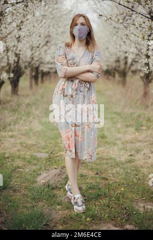 Frau zwischen blühenden Bäumen. Mädchen in einer medizinischen Maske in einem blühenden Garten. Quarantäneort. Frühling in Polen. Frühlingsgärten Stockfoto