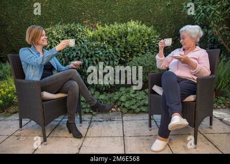 Seniorin und Pflegekraft, die Kaffee im Garten trinkt, mit Sicherheitsbedenken Stockfoto