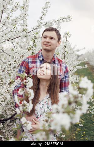 Ein junges Paar, das sich im Garten entspannt. Ein Mädchen mit einem Kerl im Garten. Verliebt auf einem Spaziergang in der Natur. Stockfoto