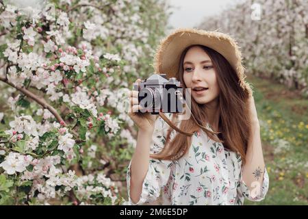 Naturfotograf, der Fotos im Freien macht. Hübsches Mädchen mit Hut und Kleid in einem Apfelgarten. Draußen vor der Stadt. Stockfoto