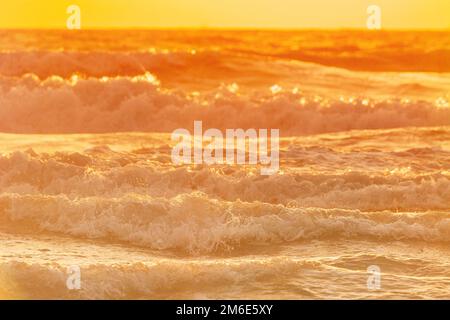 Abenduntergang über dem Meer. Riplpe Meerwasseroberfläche mit kleinen Wellen bei Sonnenaufgang. Wasserschaum spritzt. Wunderschöne Natur mit Meereslandschaft Stockfoto