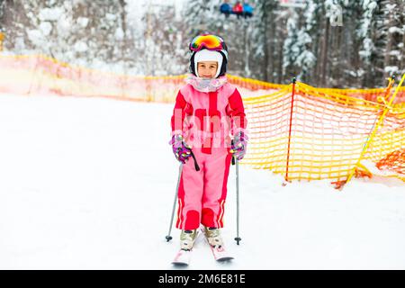 Kinder Skifahren in den Bergen. Aktives Kleinkind mit Schutzhelm, Schutzbrille und Stöcken. Skirennen für kleine Kinder. Wintersport für die ganze Familie. Kinder Ski Stockfoto