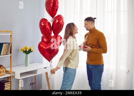 Ein junger, lächelnder, gutaussehender Mann schenkt seiner attraktiven Freundin ein Geschenk zum Valentinstag, Geburtstag, Feiertag. Stockfoto