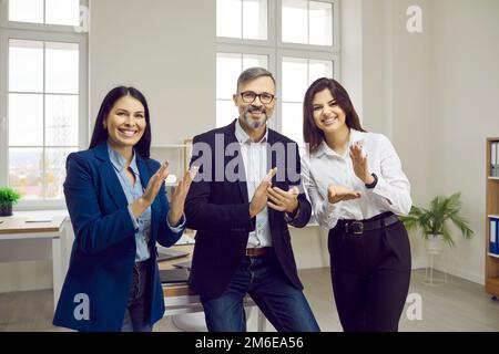 Glückliche Geschäftsleute stehen in einem modernen Büro und applaudieren Stockfoto