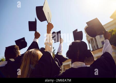 Universitätsabsolventen halten ihre akademischen Mützen bis zum hellblauen Himmel am Abschlusstag Stockfoto