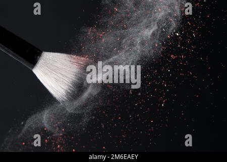Make-up-Pinsel mit zerkleinertem weißem schwimmendem Pulver und rotem Glitzer auf schwarzem Hintergrund Stockfoto