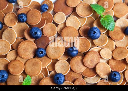 Trendiges, hausgemachtes Frühstück, Pfannkuchen, Müsli, Mini-Pfannkuchen auf hellem Teller auf rosa Betongrund Stockfoto