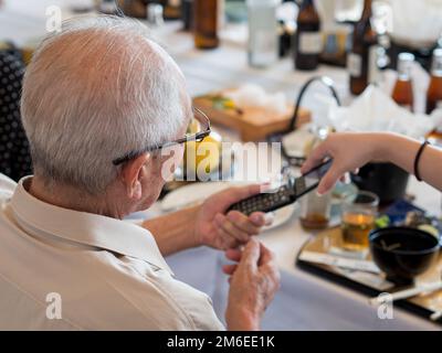 Ein älterer asiatischer Mann, der sich darum bemüht, ein altmodisches Flip-Phone zu benutzen Stockfoto