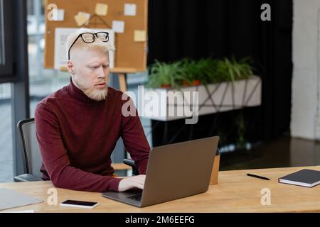 Bärtiger Albino-Geschäftsmann, der ein Laptop in der Nähe eines Smartphones benutzt, mit leerem Bildschirm im Büro, Stock-Bild Stockfoto