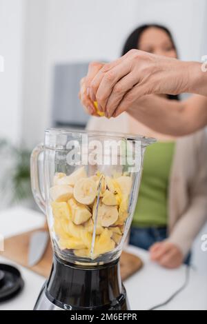 Reife Frau, die Zitrone presst, während sie mit einem Freund in der Küche Frucht-Smoothie zubereitete, Stockbild Stockfoto
