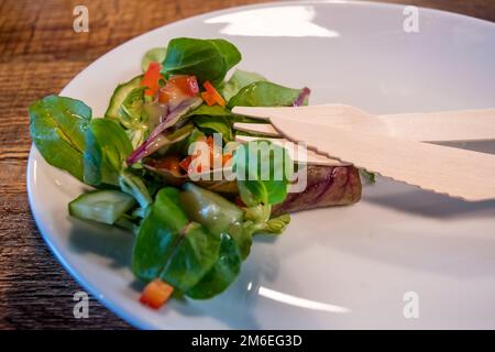 Umweltfreundliches Holzbesteck auf einem Teller mit Beilagensalat. Alternative zu weniger ökologisch freundlichem Einwegkunststoff in einem Café. Stockfoto