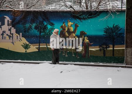 Moskau, Russland. 3. Januar 2023. Eine Frau läuft unter dem Schnee vor einem Wandgemälde, das die biblischen drei Könige (Weisen) im Kloster Vysokopetrovsky im Zentrum von Moskau, Russland, darstellt Stockfoto