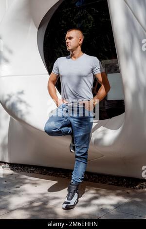 Ein Mann in der Nähe eines weißen runden Fensters. Ein Typ in Motorradschuhen. Männliches Porträt. Stockfoto