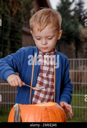 Ein Junge mit einem Kürbis. Ein kleiner Junge schneidet einen orangen Kürbis. Wir bereiten uns auf Halloween vor. Stockfoto