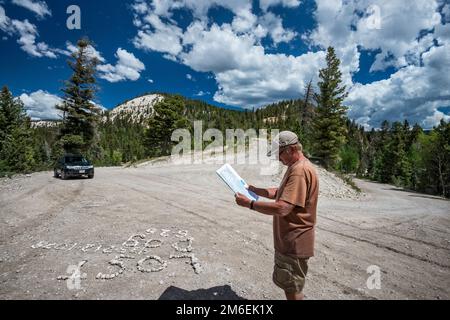 Mann überprüft Karte, Schild mit der Schrift „Lost Dog Shingle“ auf der Straßenoberfläche an der Kreuzung von FR 17, FR 143 und FR 140. Escalante Mountains, Utah, USA Stockfoto