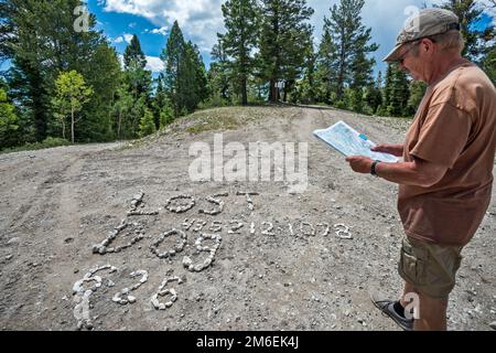 Mann überprüft Karte, Schild mit der Schrift „Lost Dog Shingle“ auf der Straßenoberfläche an der Kreuzung von FR 17, FR 143 und FR 140. Escalante Mountains, Utah, USA Stockfoto