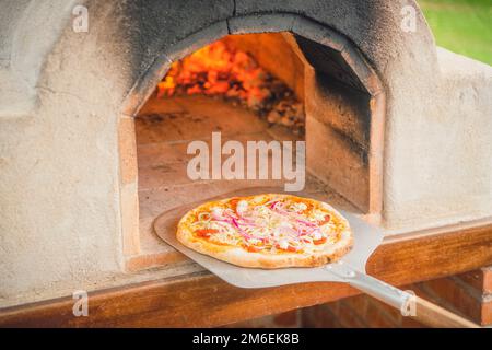 Köstliche Pizza aus einem heißen Steinofen im Freien, der mit einer Essensschaufel ausgelöscht wurde Stockfoto