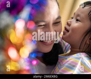 Ein kleines asiatisches Mädchen mit mom, die zusammen einen Weihnachtsbaum schmückt Stockfoto