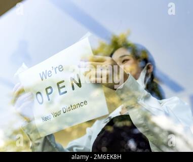 Asiatische Kellnerin, die ein Open Signage Restaurant aufsetzt Stockfoto