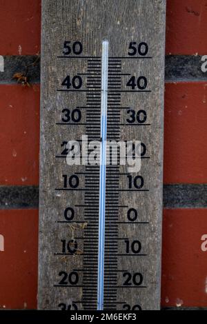 Eine Nahaufnahme eines Quecksilberthermometers aus Holz, das die Außentemperatur in Grad Celsius anzeigt und an einer roten Ziegelwand hängt. Die Messgeräte Stockfoto