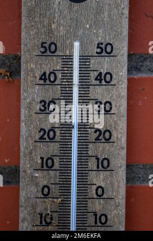Nahaufnahme eines Quecksilberthermometers aus Holz, das die Außentemperatur in Grad Celsius anzeigt und an einer roten Ziegelwand hängt. Die Mess. Stockfoto