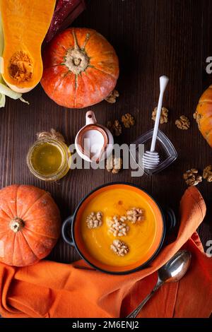 Gebackene Kürbiscreme mit Nüssen, Kokosmilch und natürlichem Honig, serviert in einer schönen Schüssel. Serviert an einem braunen Holztisch mit Riss Stockfoto