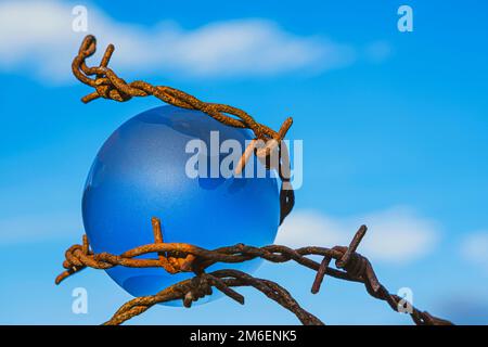 Der Begriff der Symbolik. An einem blauen Himmel befindet sich eine Glaskugel, die von rostigem Stacheldraht umgeben ist Stockfoto