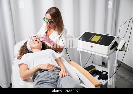 Moderne Behandlung von Teleangiektasien auf der Haut. Kosmetikerin, die lokal hochpräzise Entfernung erweiterter kleiner Gefäße im Gesicht mit innovativem gelben Laser durchführt. Stockfoto