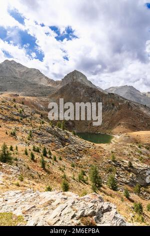 Lake Loie (Lago di Loie) und umgibt alpine Felsen mit im Herbst verwelktem gelben Gras und Zwergkiefern unter weißen Wolken. Aosta-Tal, Italien Stockfoto