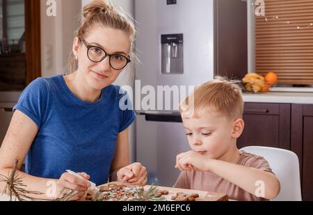 Junge Mutter und Sohn in der Küche, die Kekse backen. Weihnachten Lebkuchenmann Glasrohre Dekoration. Eine Frau mit ihrer Kinderdekorati Stockfoto