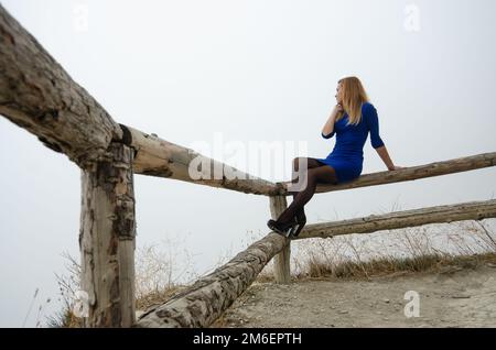 Das Mädchen sitzt auf einem Holzzaun, um das Mädchen herum ist ein fester Nebel Stockfoto