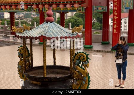 Gebete in einem Tempel. Räucherbrenner im Vordergrund, rote Säule mit chinesischem Schriftzug im Hintergrund. Malaysia, Kuala Lumpur, Thean Hou Tempel Stockfoto